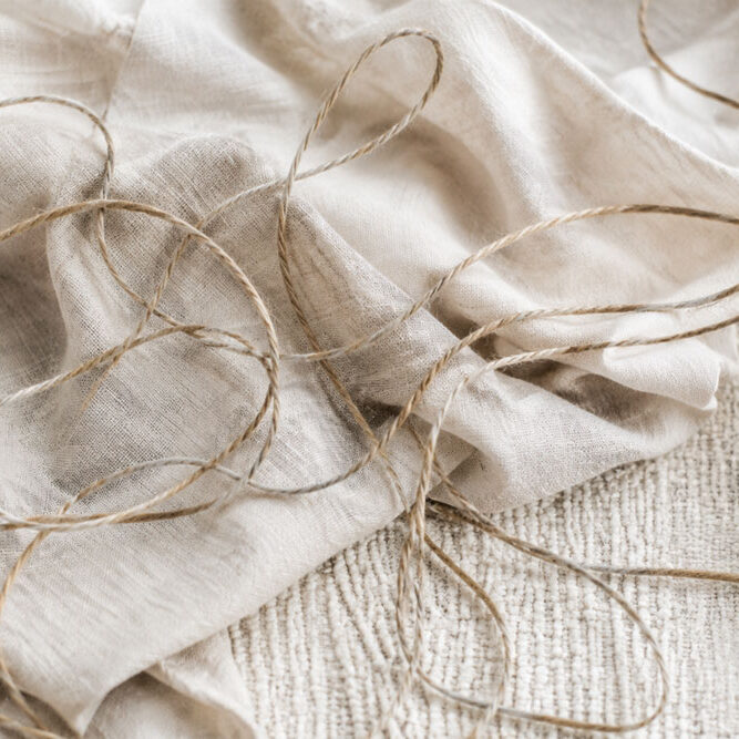 Loose natural cord resting across soft cream linen, representing invisible beliefs and inner rules.